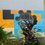 Afrocentric mural of a stylized female face with traditional headgear, set against a colorful abstract background of blue, orange, and yellow blocks with tribal textures