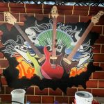 Vibrant wall mural featuring three electric guitars bursting through a brick wall, surrounded by abstract musical waves, fire elements, and urban graffiti-style art.